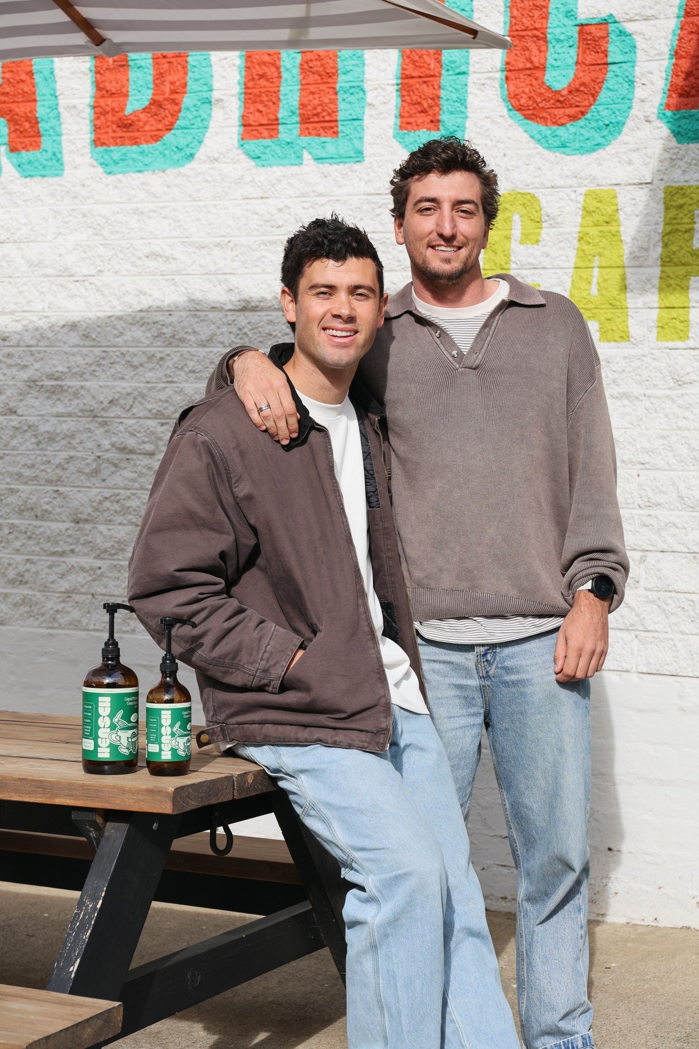 Hensch founders Nic and Nick outside a cafe with two bottles